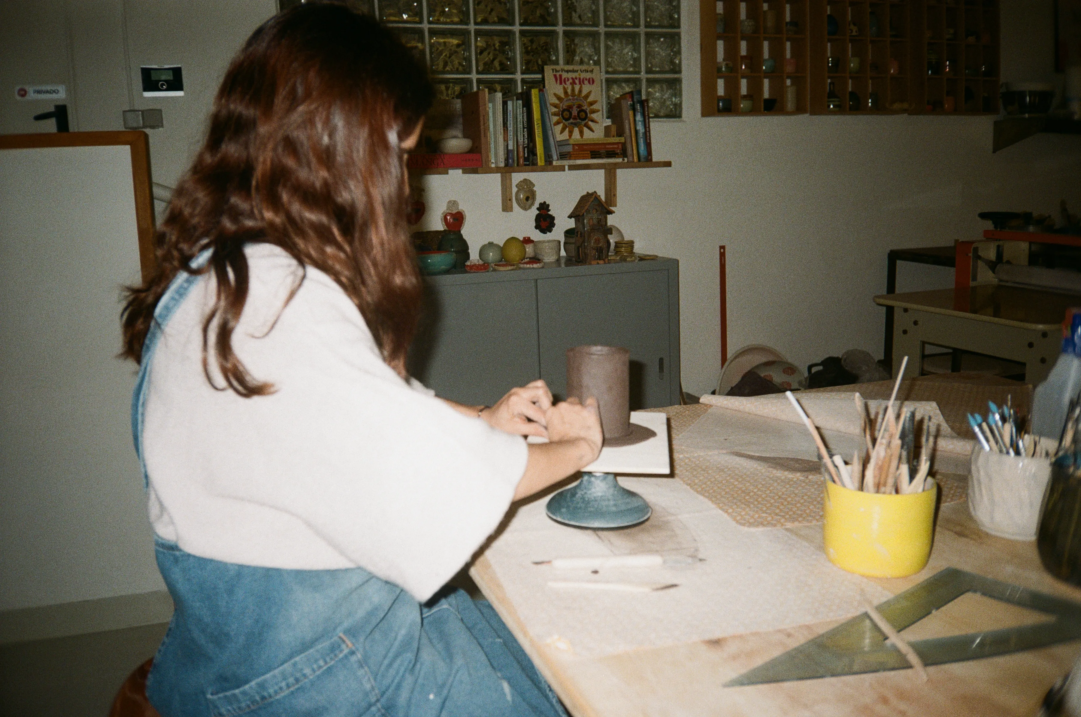 Una alumna refina una pieza cilíndrica sobre la torneta, en la mesa de modelado del estudio