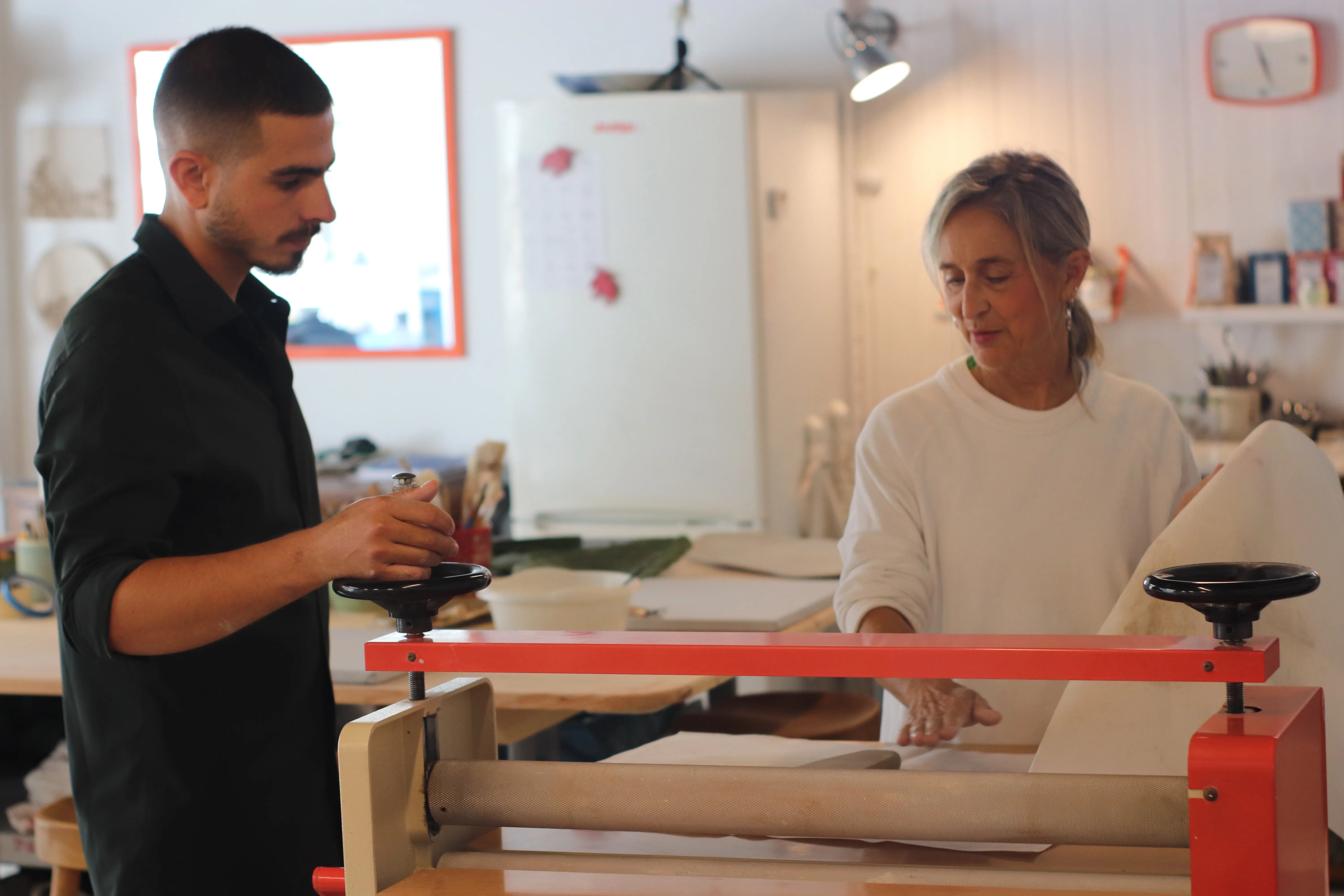 Laura y un alumno estiran una plancha de barro en la laminadora