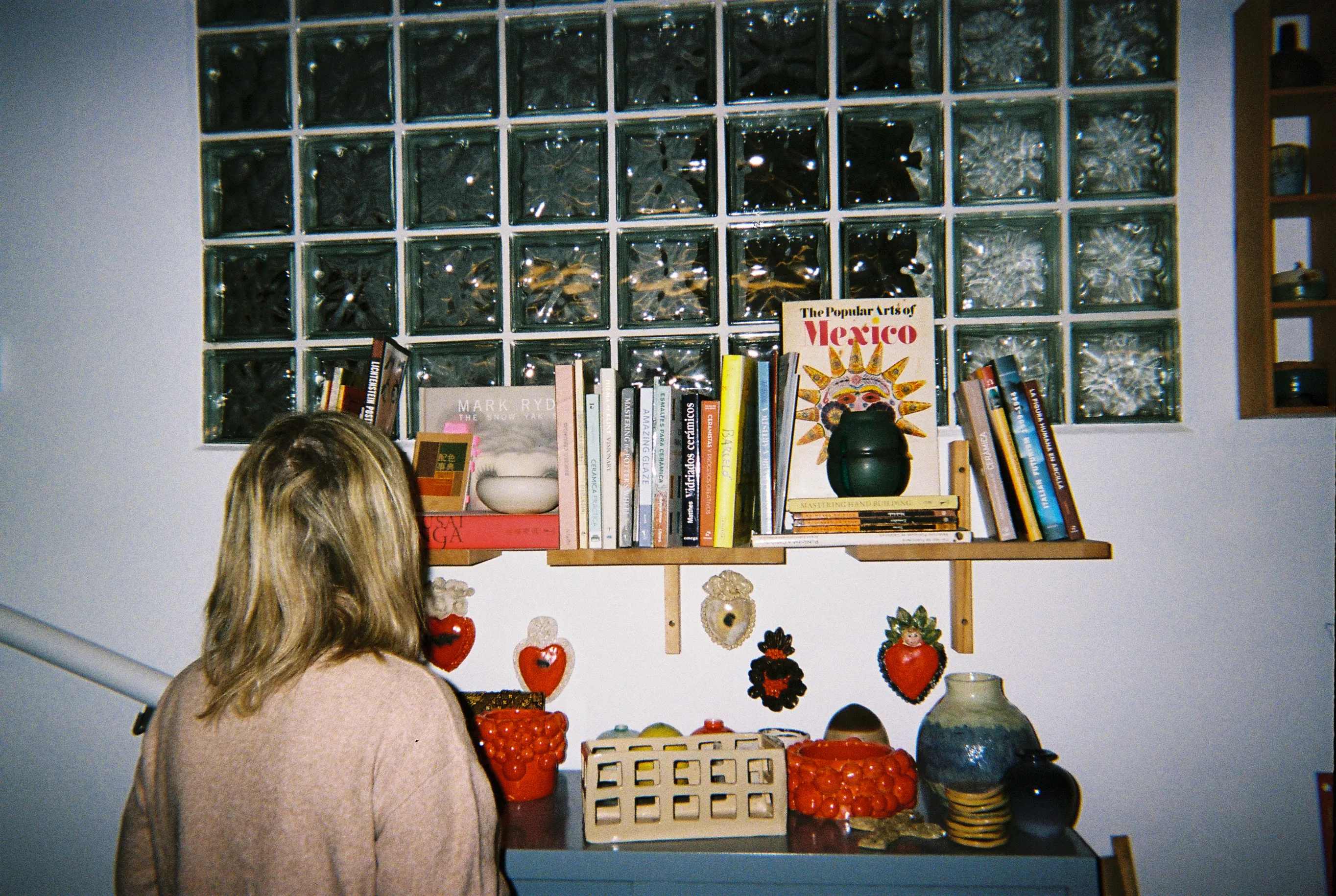 Laura frente a la pared del estudio decorada con Sagrados Corazones de cerámica bajo la estantería de libros