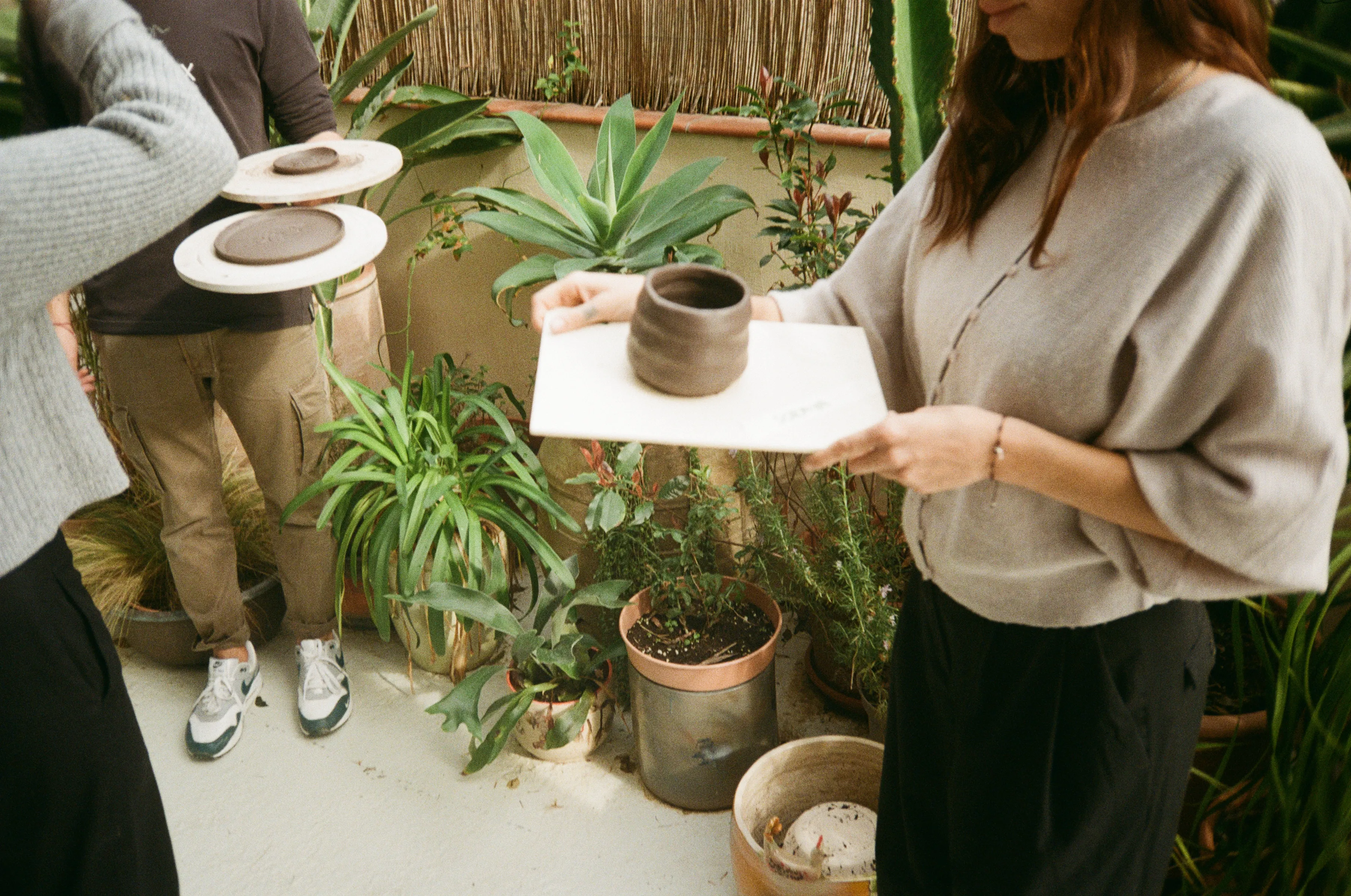 Alumnas llevando sus piezas de barro recién modeladas por el patio de plantas del estudio